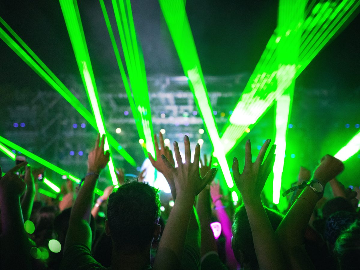 Público con las manos en alto entre haces de luz verde en un concierto